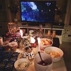 a table topped with bowls filled with food next to a flat screen tv and candles