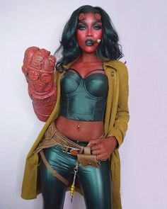 a woman with green hair and makeup is holding a red object in her hand while standing next to a white wall