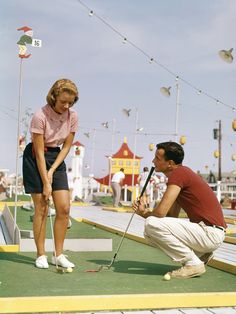 a man and woman playing miniature golf on the boardwalk