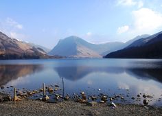 a lake surrounded by mountains with rocks in the foreground and water on the other side