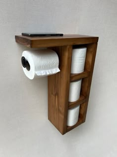 a wooden shelf with two rolls of toilet paper hanging from it's sides and a laptop on top