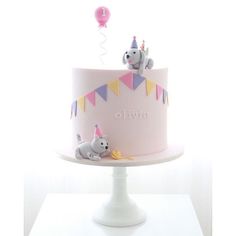 a pink cake with elephants on top and balloons in the air, sitting on a white pedestal