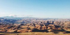 an aerial view of hills and valleys in the distance, with mountains in the background