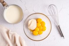 eggs, sugar and milk are on a plate next to a whisk in a glass bowl