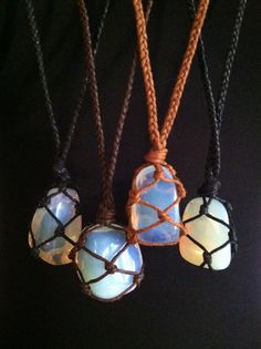 four necklaces with different colored glass beads hanging from cords on a black background in the dark