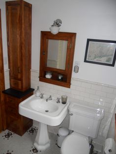 a bathroom with a toilet, sink and mirror in it's corner area next to a cabinet