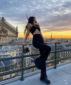 a woman standing on top of a balcony next to a railing with buildings in the background