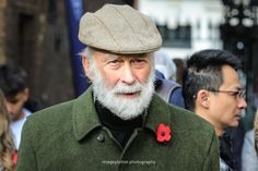 an older man with a white beard wearing a green coat and a red flower on his lapel