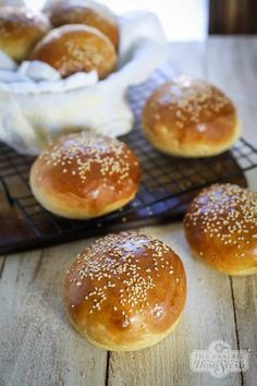 small buns with sesame seeds on a cooling rack next to a basket of rolls