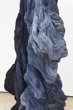 an abstract sculpture made out of blue and black rocks on a wooden floor in front of a white wall