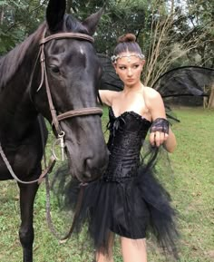 a woman in a black dress is standing next to a horse and posing for the camera