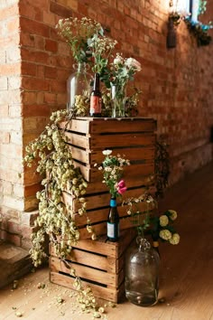 a wooden crate with flowers and bottles sitting on the floor in front of a brick wall