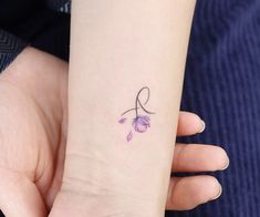 a small tattoo on the wrist of a woman's left arm, with a purple flower