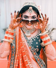 a woman in an orange and black outfit holding her hands up to her face with henna on