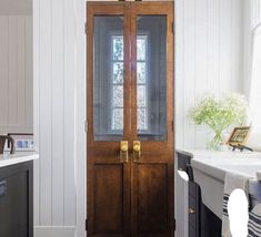 a wooden door in the middle of a kitchen with white walls and floor tiles on the floor