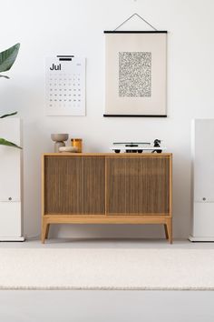 a wooden cabinet sitting in front of a white wall next to a plant and pictures