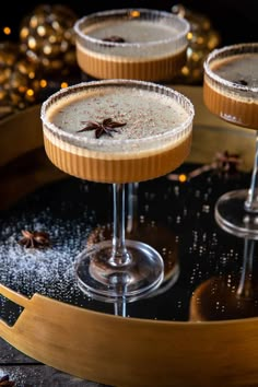 three glasses filled with drinks sitting on top of a wooden tray next to christmas decorations