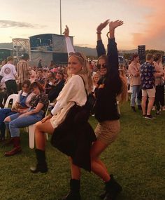 two women dancing in front of an audience at a music festival with their arms up