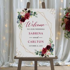 a welcome sign with flowers on it in front of a white curtain and lights behind it