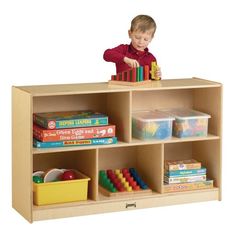 a young boy standing on top of a wooden book shelf filled with books and toys