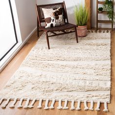 a room with a chair, rug and plant in the corner on the wooden floor