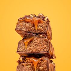 three pieces of chocolate cake with caramel drizzled on top, stacked up against an orange background