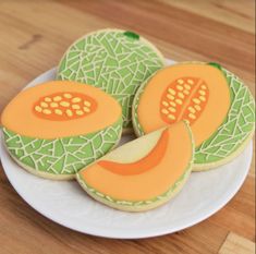 three decorated cookies sitting on top of a white plate next to an orange and green piece of fruit