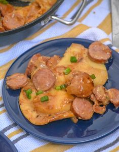 a blue plate topped with food next to a pan filled with chicken and sausages