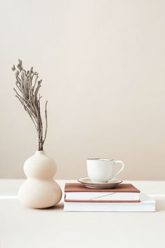 a cup and saucer sitting on top of books next to a vase with branches in it