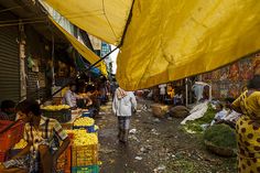 people are shopping at an outdoor market with yellow awnings over the vendors'stalls