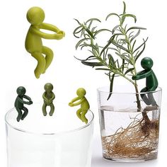 three small figurines are sitting next to a plant in a glass vase with water