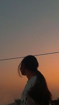 a woman flying a kite in the sky at sunset or dawn with her hair blowing back