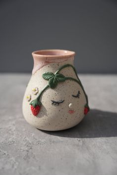 a small ceramic vase with a face painted on it's side, sitting on a table