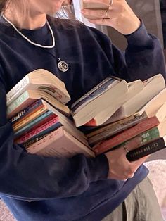 a woman sitting on a couch holding a stack of books and drinking from a cup