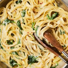 a pan filled with pasta and spinach on top of a wooden spoon in it