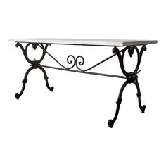 a wrought iron table with marble top and two small scrolls on the legs, against a white background