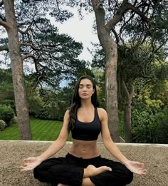 a woman is sitting in the middle of a yoga pose with two trees behind her