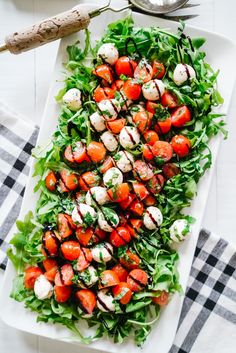 a salad with tomatoes and mozzarella cheese on a white platter next to a fork