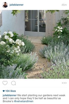 a garden with lavender and white flowers in front of a house that has an open door