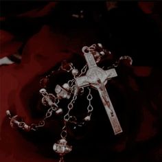 a rosary and some beads on a red cloth with a black cross in the background