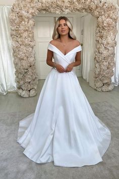 a woman wearing a white wedding dress standing in front of a floral arch with her hands on her hips