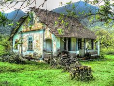 an old house sitting in the middle of a lush green field with mountains in the background