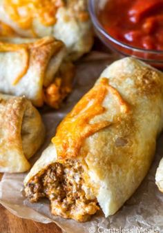 some taco stuffed pastries are sitting on wax paper with sauce in the background