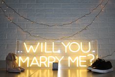 a lighted sign that says will you marry me? and some shoes on the table