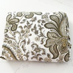 a white and brown paisley print pocket square on a marble countertop with gold accents