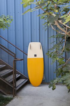 a yellow and white surfboard sitting in front of a blue building with stairs leading up to it