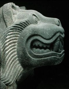 a stone carving of a dragon head with its mouth open and teeth wide open, in front of a black background