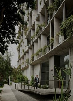 a man walking down a sidewalk next to a tall building with plants growing on it