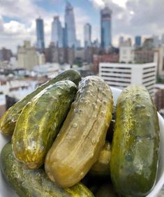 a white bowl filled with cucumbers in front of a cityscape and skyscrapers