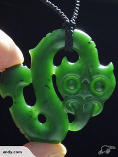 a hand holding a green pendant with a face on it